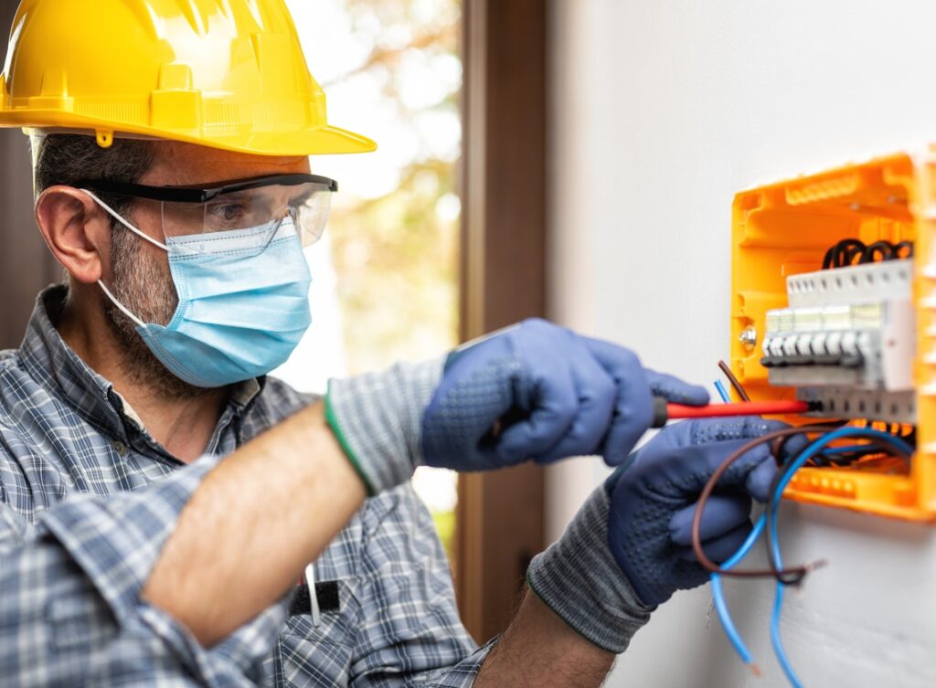 Electrician at work with face protected by surgical mask to prevent Coronavirus infection. Covid-19 pandemic.